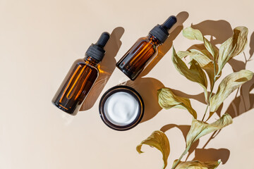 Face and eye moisturizer cream and serum in a glass bottles and jar and dried herb on light beige...