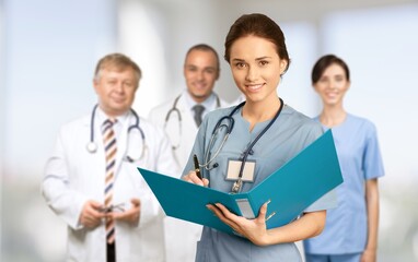 Fototapeta premium Portrait of happy young nurse in uniform with healthcare team in background. Successful doctor and nurses