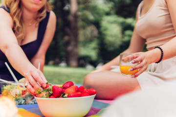 Close up of a woman's hand picking strawberries at a picnic with friends, eating, outdoors