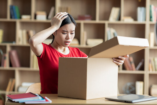 Upset unhappy teenager asian female look at cardboard box in living room interior