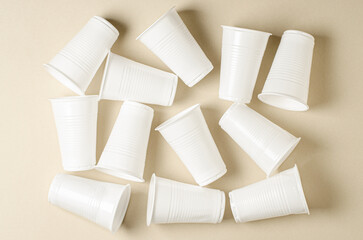 Disposable white plastic tableware on a beige background. The concept of nature pollution