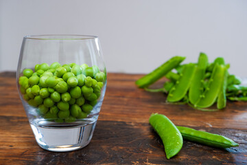 Green peas in glass bowl. fresh pea in the pod with green leaves. green peas on a brown wodden table