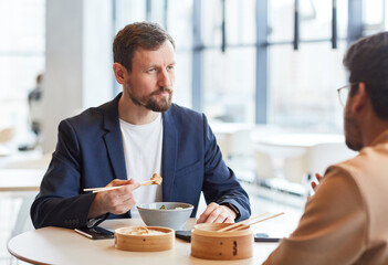 Portrait of bearded businessman enjoying Asian food during business lunch with colleague at shopping mall cafe