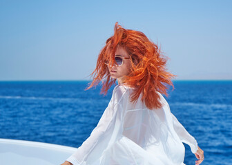 Portrait of red hair girl posing on the edge of white yacht, arms outstretched in different...