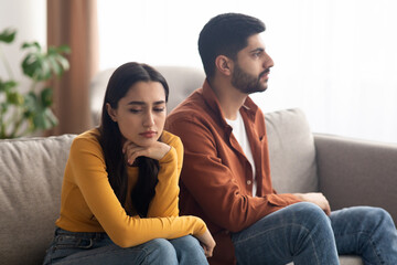 Obraz premium Unhappy Arabic Couple Sitting On Couch Indoor, Having Relationship Problems