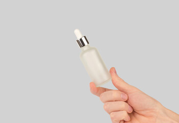 Male hand holding a bottle of hair serum. White cosmetic bottle with a pipette in a man's hand.