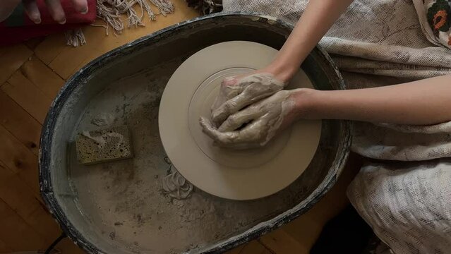 Top view of female hands, soiled in clay, working on potters wheel. Woman learning ceramic art at workshop studio