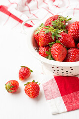 Aerial view of strawberries in a white colander on a white table with a red kitchen cloth, white background, vertical, with copy space