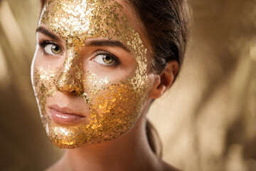 Beautiful woman with golden shining mask on her face for skin treatment
