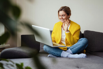 Young happy woman waving into laptop camera during online conversation by video call