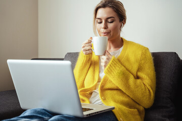 Woman with cup of hot coffee sitting on the sofa and using laptop computer at home