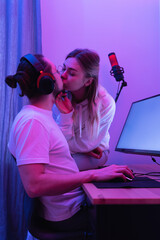 Young couple kissing at the table with gaming personal computer in neon light