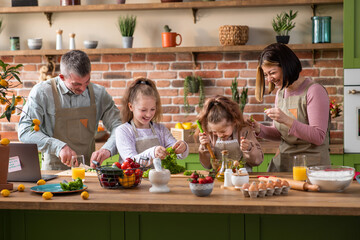 At home in the kitchen large and luminous happy and good looking family mom , dad and two daughters preparing the breakfast together they discussing and smiling large.