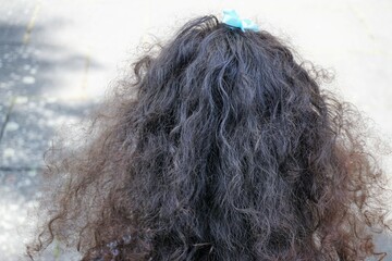 Hinterkopf von kleinem Mädchen mit langem schwarzem lockigen Haaren und blauer kleiner Schleife...