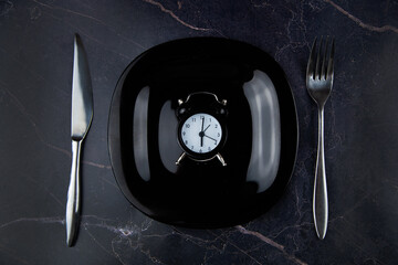 Inside the black plate is a black alarm clock, on the sides are devices on a dark background. High...