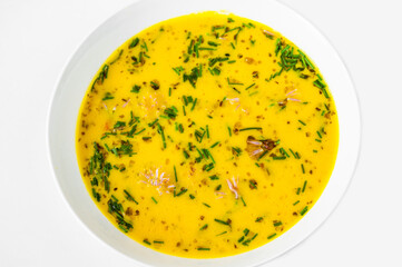 Creamy yellow vegetable soup in white plate on white.