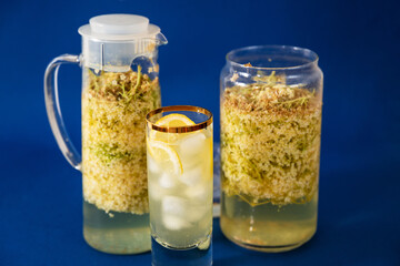 Preparation of elderberry sirup in 2 glasses, drink with ice on blue.