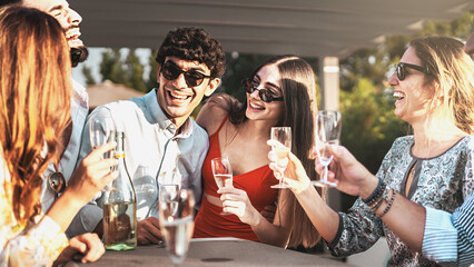 Happy friends with sunglasses cheering and drinking champagne at garden party outdoor - Young millennials people having fun at weekend afternoon - Youth lifestyle and nightlife concept © Lomb