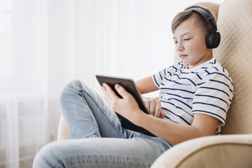 Teenage boy in wireless headphone using tablet having video chat on internet online at home. Child watching movie, playing video game. Social media concept. Online education. Distance learning