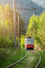 Fototapeta premium an old atmospheric tram in the forest against the background of mountains, an interesting colorful route train red wagon at the foot of the mountain in Russia Khakassia