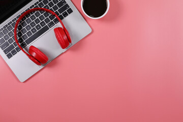 Red headphone placed on laptop with black coffee cup isolated on pink background. Flat lay...