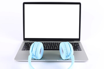light blue headphones placed on a laptop isolated on a white background with copy space on the computer screen.