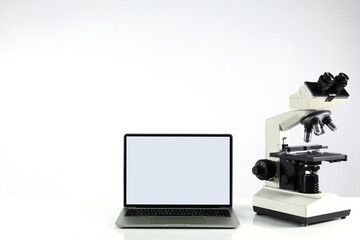 Concept of research and development of microscopes in science laboratories. There is a laptop on the table and a white background.