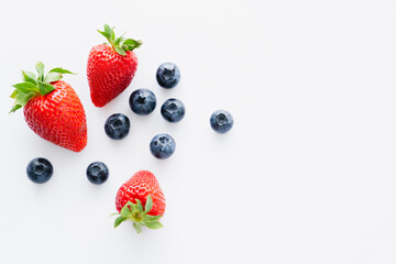 Top view of blueberries and strawberries with green leaves on white surface.