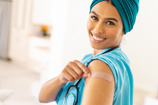 Portrait of smiling biracial young female doctor in hijab showing bandage on arm at clinic