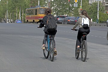 Two girls ride bicycles on the sidewalk on a spring day