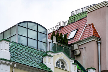 Fototapeta na wymiar Glazed conservatory garden on terrace with thuja and red roof with skilight windows, gutters and drainpipes of city residential house