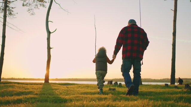 little boy is spending time with grandfather in nature, old fisher and child are going to river shore for fishing