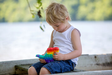 Little toddler child, blond boy, playing with pop it antistress toy in the park in a boat - obrazy, fototapety, plakaty