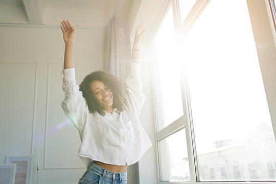 Carefree Joyful African American Girl Jumping Dancing Alone Moving To Rhythm In Living Room, Happy African American Young Woman Have Fun Enjoying Listening To Music, Entertain On Weekend At Home      