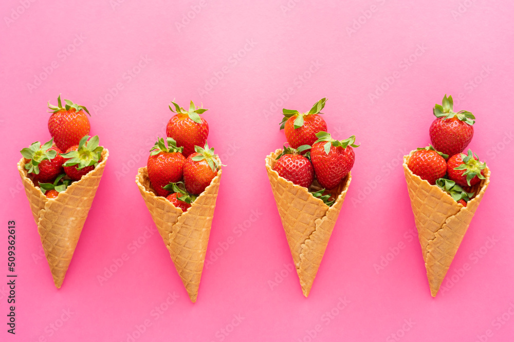 Sticker Flat lay with ripe berries with leaves in waffle cones on pink background.