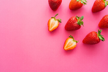 Top view of whole and cut strawberries on pink background.