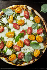 Pizza with cherry tomatoes, mozzarella and basil pesto. Dark wooden background. Top view. 