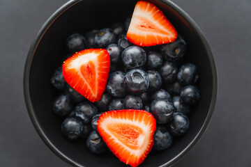 Top view of red strawberries and blueberries in bowl on black background.
