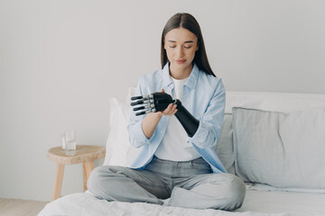Disabled young woman is assembling electronic control prosthesis. Artificial arm adjusting.