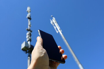 Male hand with smartphone on background of cell towers. Mobile telecommunication equipment, phone...