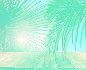 Palm branches and wooden table against light background, toned in turquoise with fade effect....