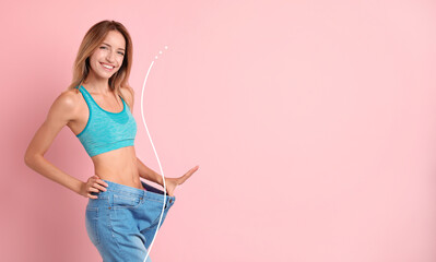 Happy young woman with slim body in oversized jeans on pink background, space for text. Weight loss - obrazy, fototapety, plakaty