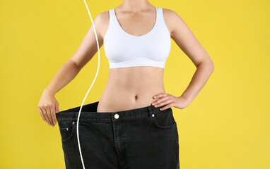 Closeup view of woman with slim body in oversized jeans on yellow background. Weight loss