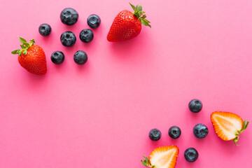 Top view of strawberries and whole blueberries on pink surface.