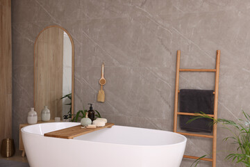 Modern ceramic bathtub, tray with toiletries and mirror indoors. Interior design