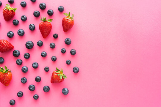 Flat lay with blueberries and strawberries on pink surface.