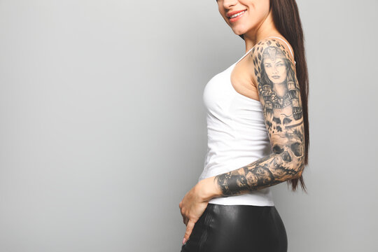 Beautiful woman with tattoos on arm against grey background, closeup. Space for text
