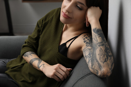 Beautiful woman with tattoos on arms resting in living room, closeup