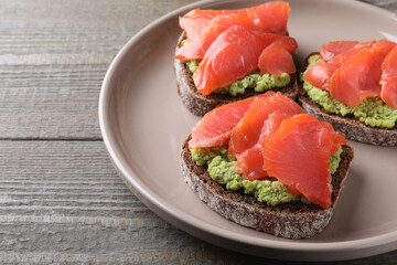 Delicious sandwiches with salmon and avocado on grey wooden table, closeup
