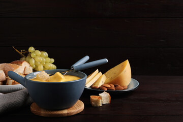 Pot of tasty cheese fondue and snacks on wooden table. Space for text